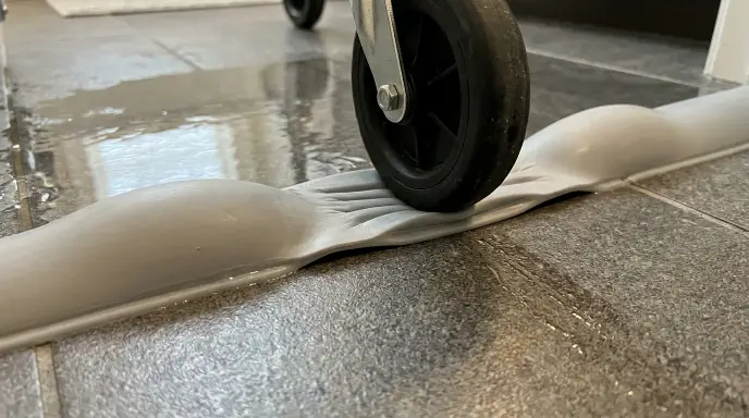 Collapsible silicone water retainer dam flattening under wheelchair wheels at curbless shower entrance