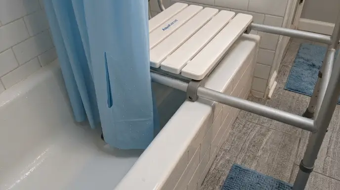 Vertical slit plastic shower curtain liner fitted cleanly around a transfer bench seat frame to prevent water leaks