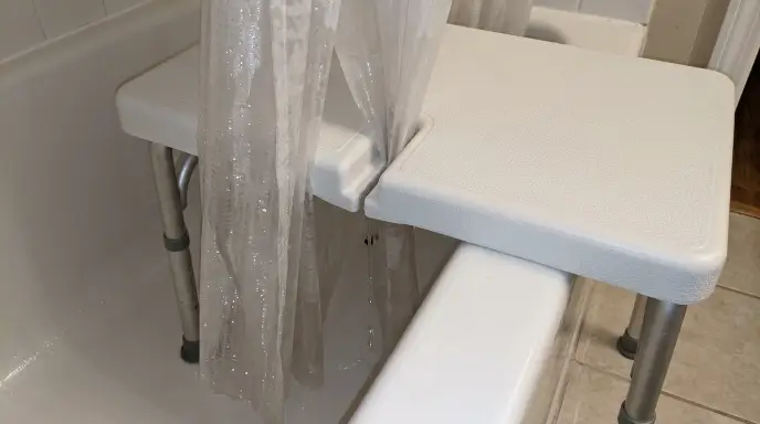 Close-up of a shower curtain tucked through a transfer bench seat slot into the bathtub to prevent water pooling on the floor